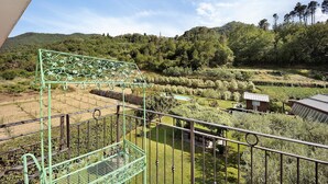 A balcony with a metal railing overlooking a garden with trees and a small building.
