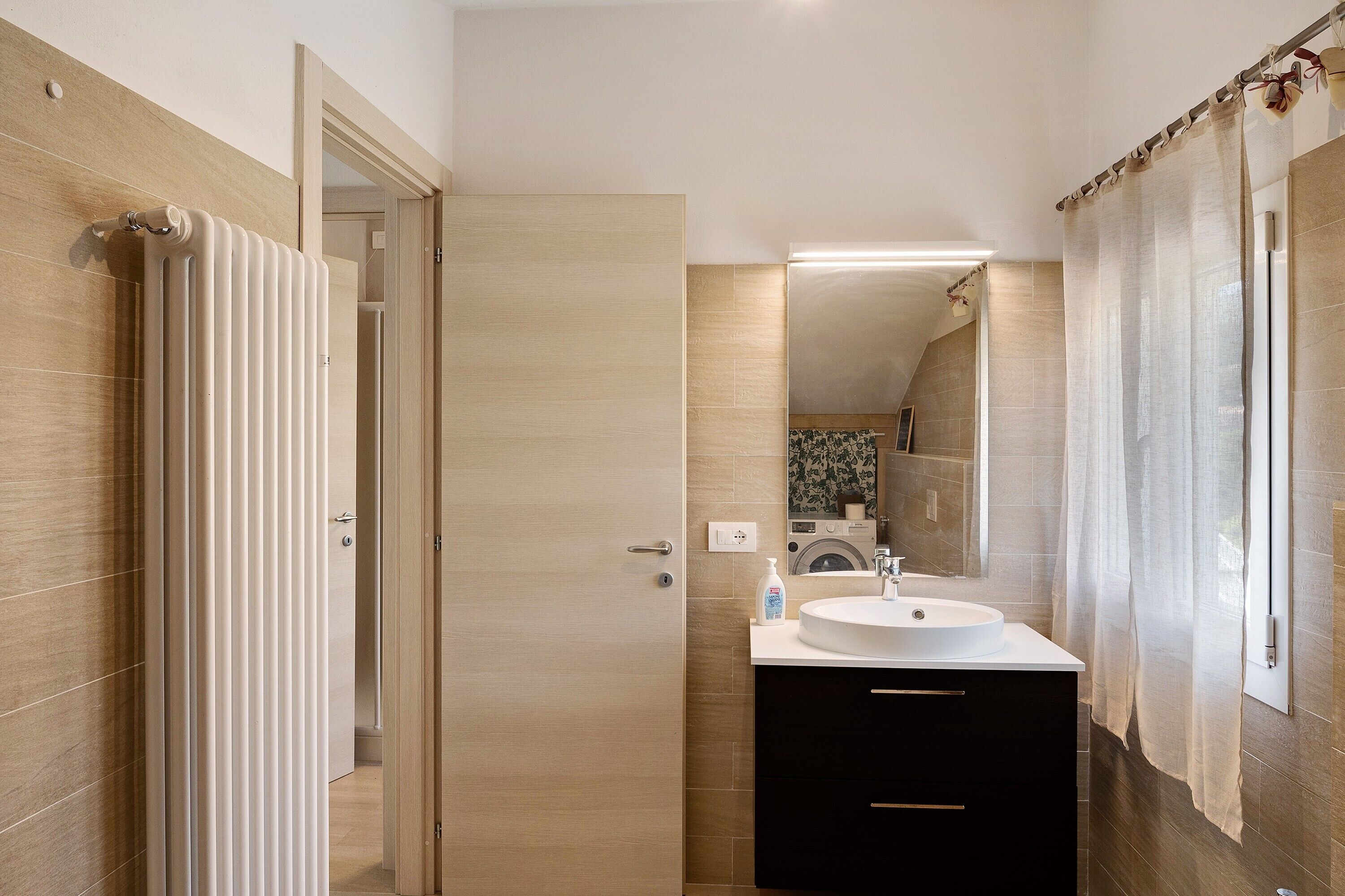 A modern bathroom with a white sink, black cabinet, and a mirror above it.