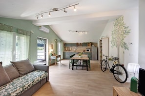 A spacious living area with a sofa, dining table, and chairs, a kitchen in the background, and a bicycle.