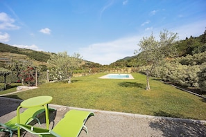 A pool with a surrounding grassy area, a small table, and chairs in the foreground.