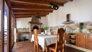 Une cuisine rustique avec une cheminée en pierre, des poutres apparentes en bois au plafond et un sol carrelé.