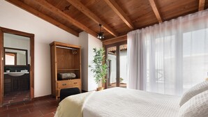 Une chambre avec un lit, des poutres en bois au plafond, une plante en pot et une vue par la fenêtre.