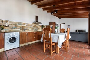 Une cuisine équipée d’un lave-linge, de meubles en bois, d’un plan de travail carrelé et d’un coin repas avec une table et des chaises.