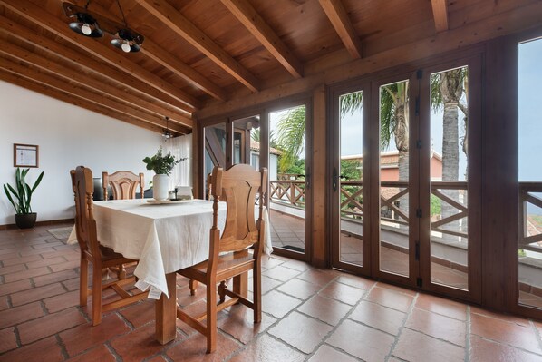 Un coin repas avec une table et des chaises en bois, une plante en pot, et une vue sur une terrasse extérieure, accessible par de grandes portes vitrées.