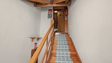 A wooden staircase with patterned tiles leading to a room with a wooden ceiling and a fire extinguisher on the wall.