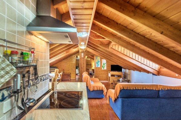 An attic-style room with a kitchen, dining area, and seating.