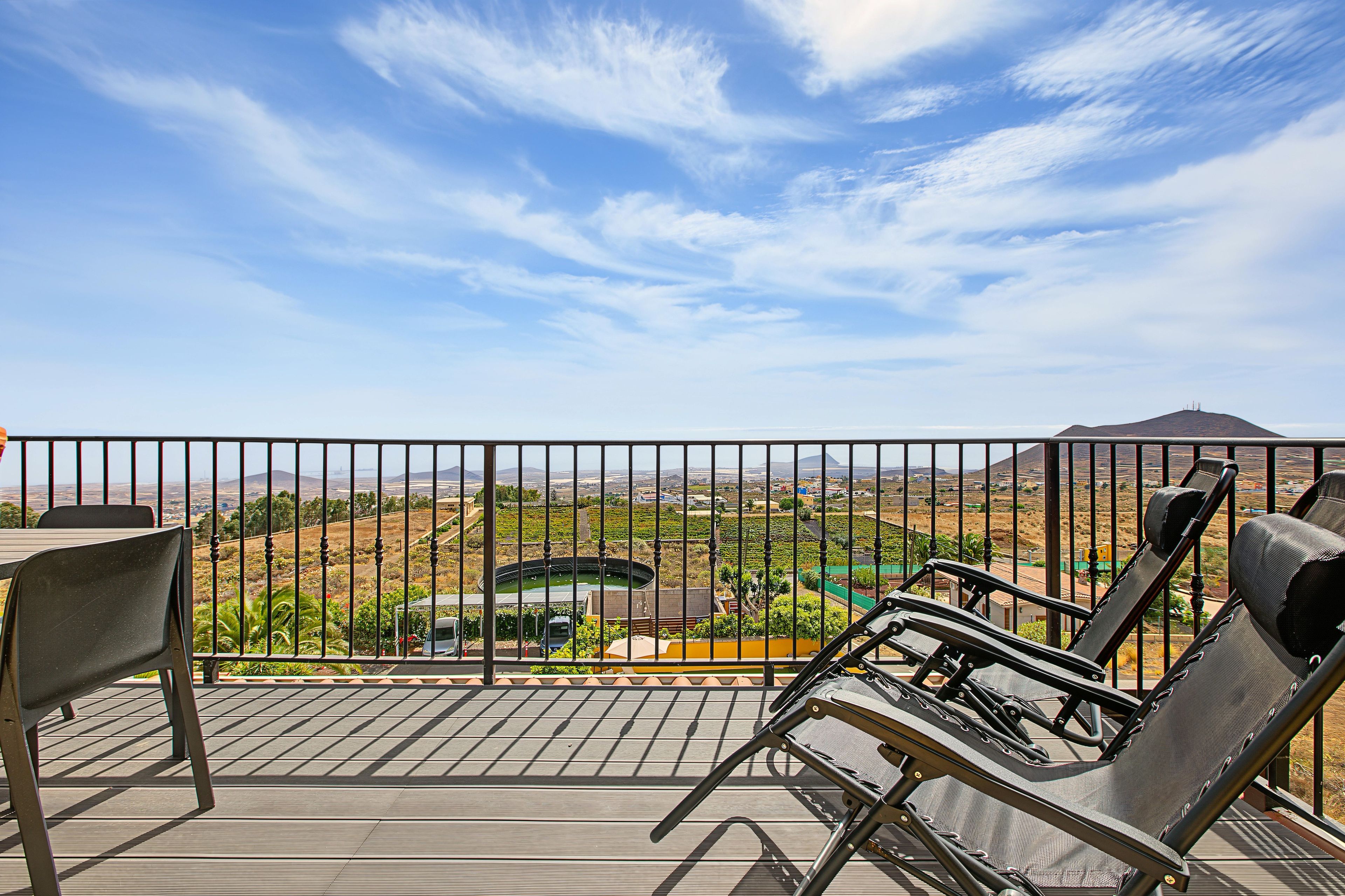 A balcony with a view of a vineyard and distant mountains.