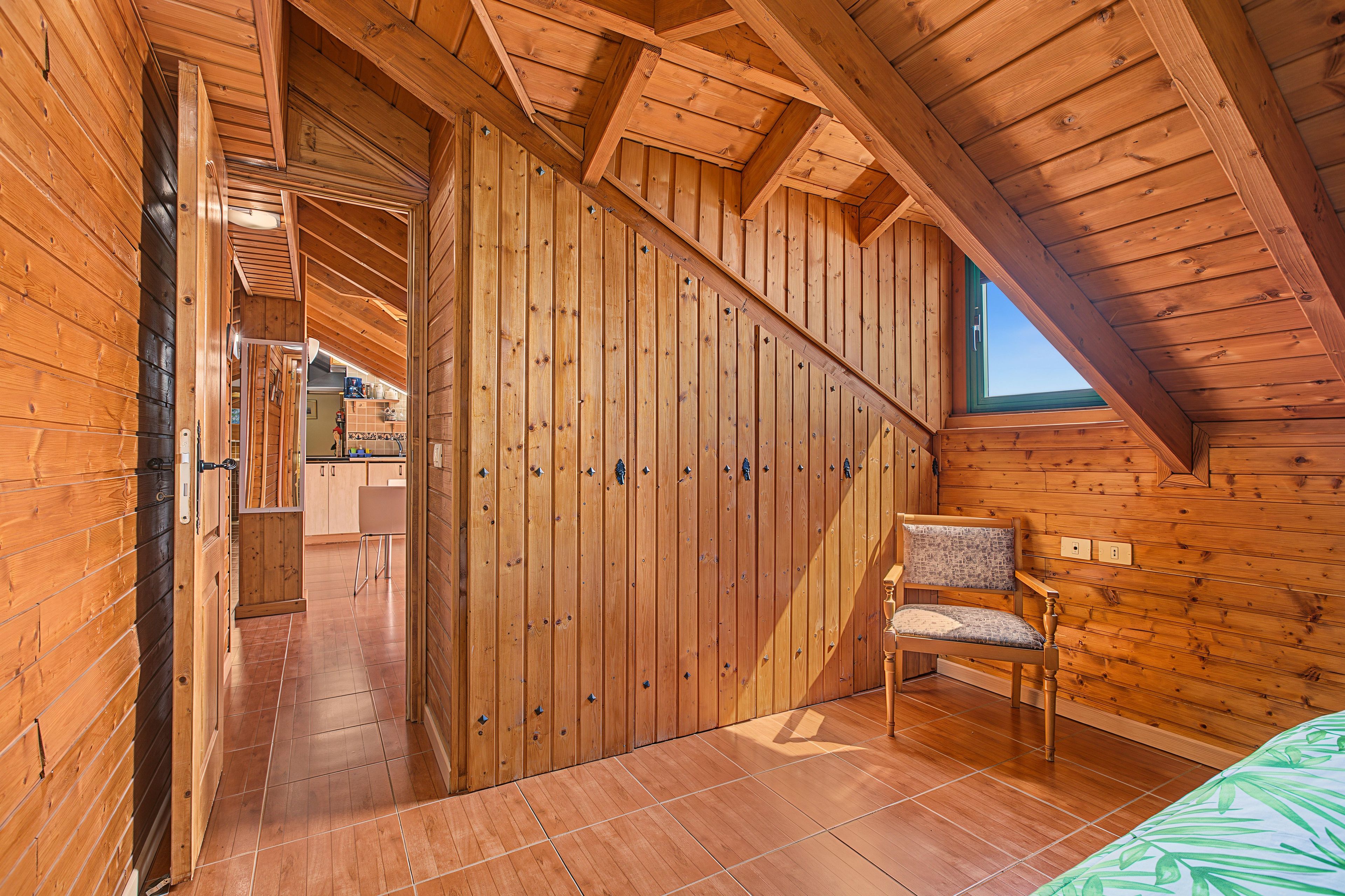 Un intérieur en bois avec un plafond en pente, une chaise et un lit.