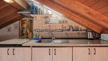 Een keuken met een schuine balkenplafond, een spoelbak en verschillende keukengerei op planken.