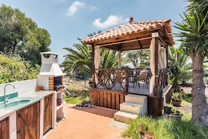 An outdoor kitchen with a grill, sink, and wooden deck with chairs.