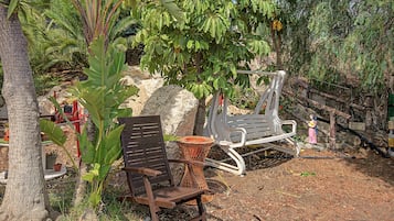 Un espace aménagé en jardin avec un banc en bois, une chaise en métal et un grand rocher.