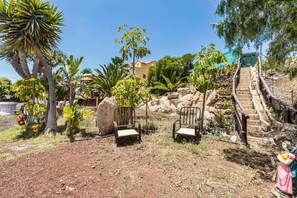 A garden with palm trees, chairs, and a statue.