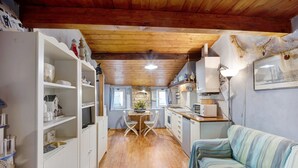 A cozy kitchen with wooden beams, white cabinets, a dining table with chairs, and a striped sofa. - Apartment "Mansarda Dei Pescatori" Near Harbour (Imperia)