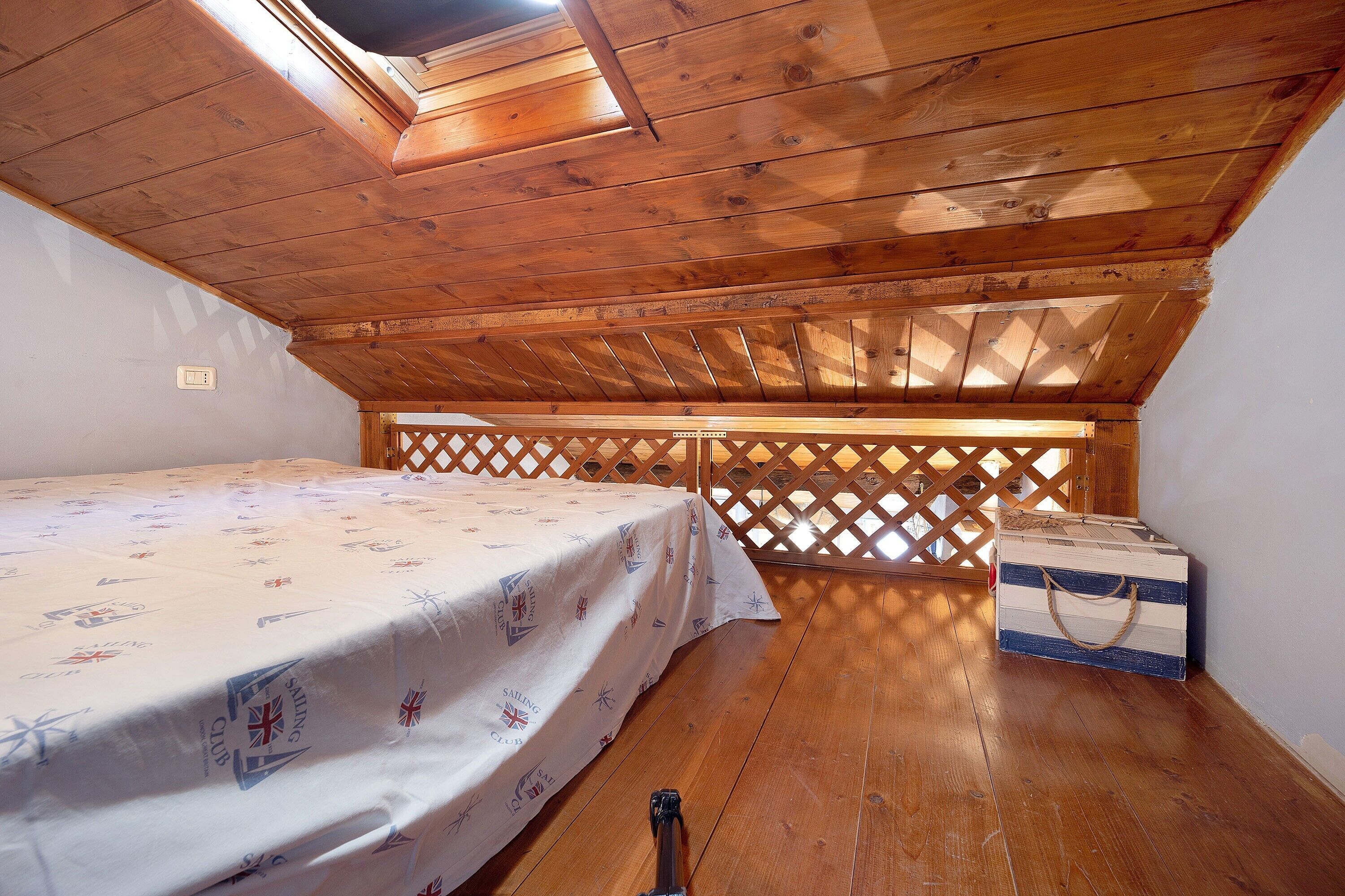 A room with a wooden ceiling, a bed with a sailboat-themed bedspread, a chest of drawers, and a lattice partition.