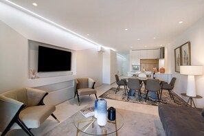 A modern living room with a flat-screen TV, comfortable seating, a dining area, and a kitchen in the background. - "Apartamento Albufeira Prestige" with Pool, Wi-Fi & Garden (Albufeira)