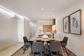 A modern dining area with a rectangular table, four chairs, and a kitchen in the background. - "Apartamento Albufeira Prestige" with Pool, Wi-Fi & Garden (Albufeira)