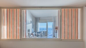 A room with a large window, a bed, and a view of the sea.