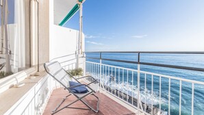 A balcony with a metal railing, a folding chair, and a view of the ocean.
