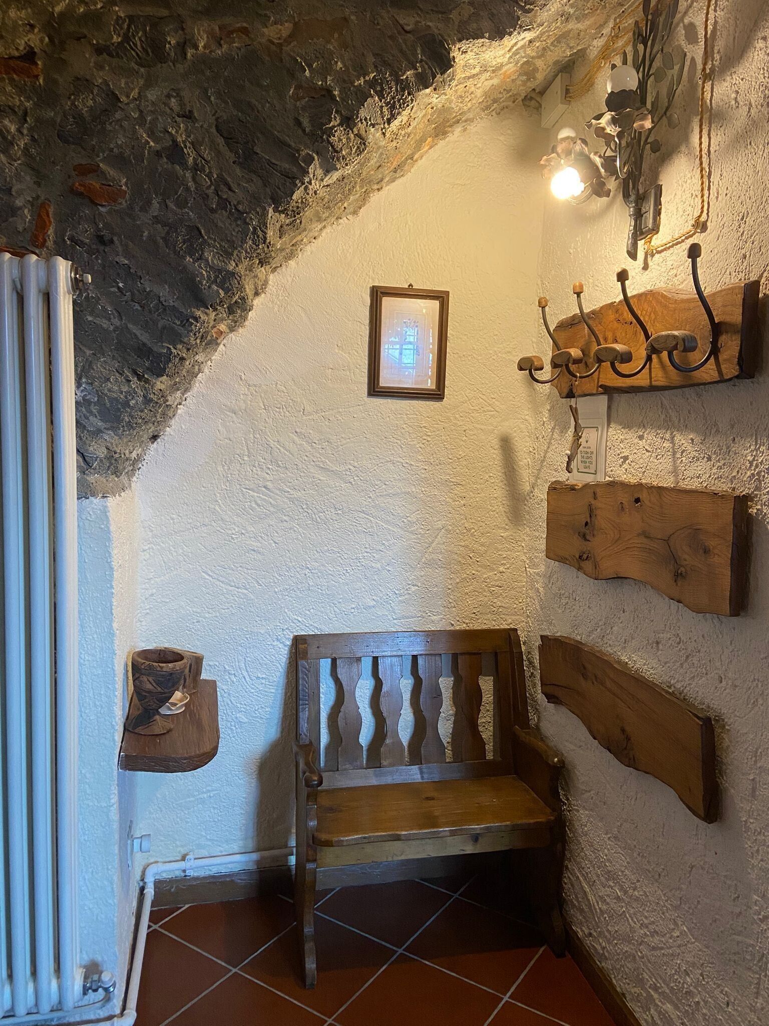 A rustic interior with a wooden bench, a wall-mounted coat rack, a framed picture, and a radiator.