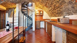 A rustic kitchen with a stone ceiling, a wooden table with a bottle of wine, a spiral staircase, and a microwave on the counter. - Holiday Home 'Cascina Taronico' with Lake View and Wi-Fi (Bellagio)