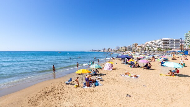 Ein Strand mit Menschen, die sich sonnen, Sonnenschirmen und einer Stadtansicht im Hintergrund.