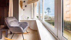 Ein modernes Zimmer mit Schaukelstuhl und großem Fenster mit Blick auf einen Strand.