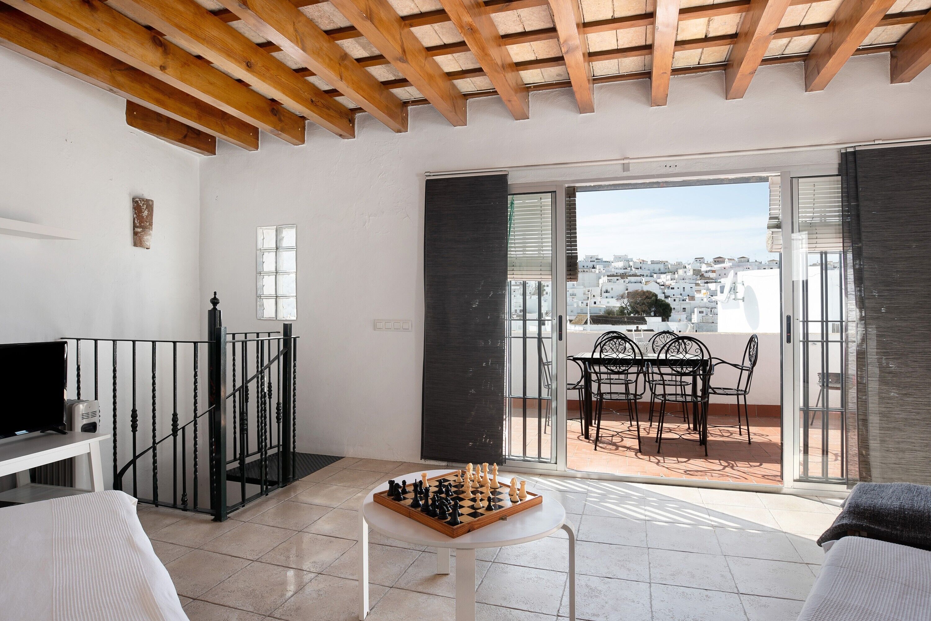 Un balcon avec une table et des chaises, un jeu d’échecs et un téléviseur posé sur un meuble.
