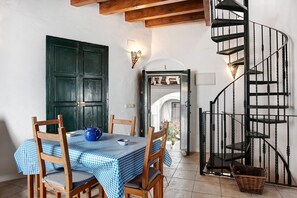 Un coin repas avec une nappe à carreaux, des chaises en bois, une théière bleue et un escalier en colimaçon noir.
