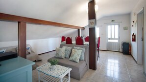 A living room with a sofa, a small table with a plant, and a dining area with red chairs. - Apartment 'Quinta Das Andorinhas - Nazaré' with Mountain View, Private Pool and Wi-Fi (Casais Baixo)