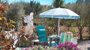 A garden with a statue, a blue umbrella, and a chair. - Apartment 'Quinta Das Andorinhas - Nazaré' with Mountain View, Private Pool and Wi-Fi (Casais Baixo)