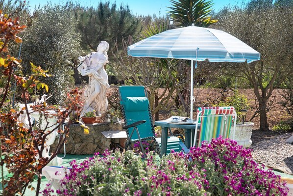 A garden with a statue, a blue umbrella, and a chair.