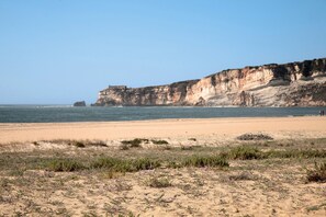 A beach with a cliff and a small structure in the distance.