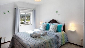 A bedroom with a bed, a window, a bedside lamp, and a wall-mounted light fixture. - Apartment 'Quinta Das Andorinhas - Nazaré' with Mountain View, Private Pool and Wi-Fi (Casais Baixo)