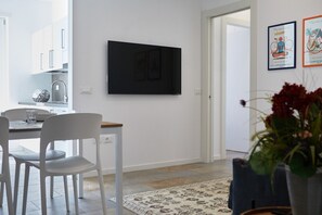 A modern kitchen with white cabinets, a dining table with chairs, a flat-screen TV mounted on the wall, and a patterned rug on the floor. - Holiday Apartment "Iris" close to Lake Garda with Wi-Fi & Garden (Riva Del Garda)