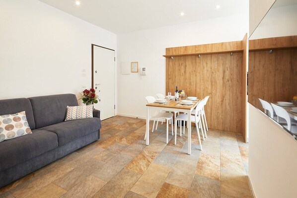 A modern living room with a grey sofa, white dining table, and chairs. - Holiday Apartment "Iris" close to Lake Garda with Wi-Fi & Garden (Riva Del Garda)
