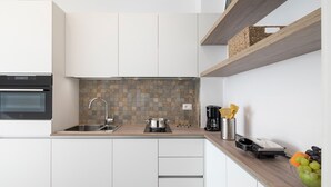 Een moderne keuken met witte kasten, een betegelde spatwand, een ingebouwde oven, een spoelbak en een koffiezetapparaat.