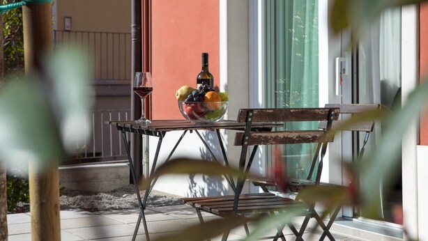 Een tafel met een schaal fruit, een fles, een glas rode wijn en een stoel voor een gebouw.