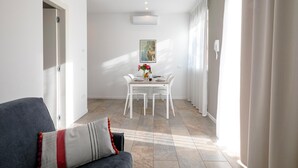 Een moderne woonkamer met een bank, een eettafel met stoelen, een schilderij aan de muur en een airconditioner.
