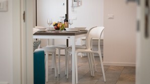A modern dining area with a table set for two, white chairs, a bowl of fruit, wine glasses, and a bottle of wine.