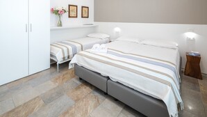 A hotel room with a large bed, a smaller bed, a wardrobe, a vanity with a mirror, and a small table with a lamp.
