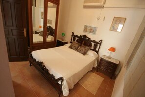 Un dormitorio con cama, mesita de noche, cómoda, espejo y aire acondicionado instalado en la pared.
