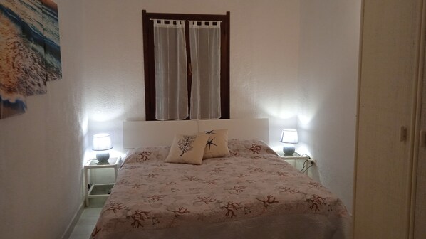 A bedroom with a bed, two bedside lamps, a window with curtains, and a wall-mounted painting.