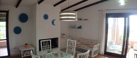 Una habitación con una mesa de vidrio, sillas blancas, un sofá, un televisor y decoración en la pared.