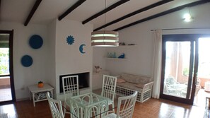 A room with a glass-top table, white chairs, a sofa, a TV, and decorative wall art.