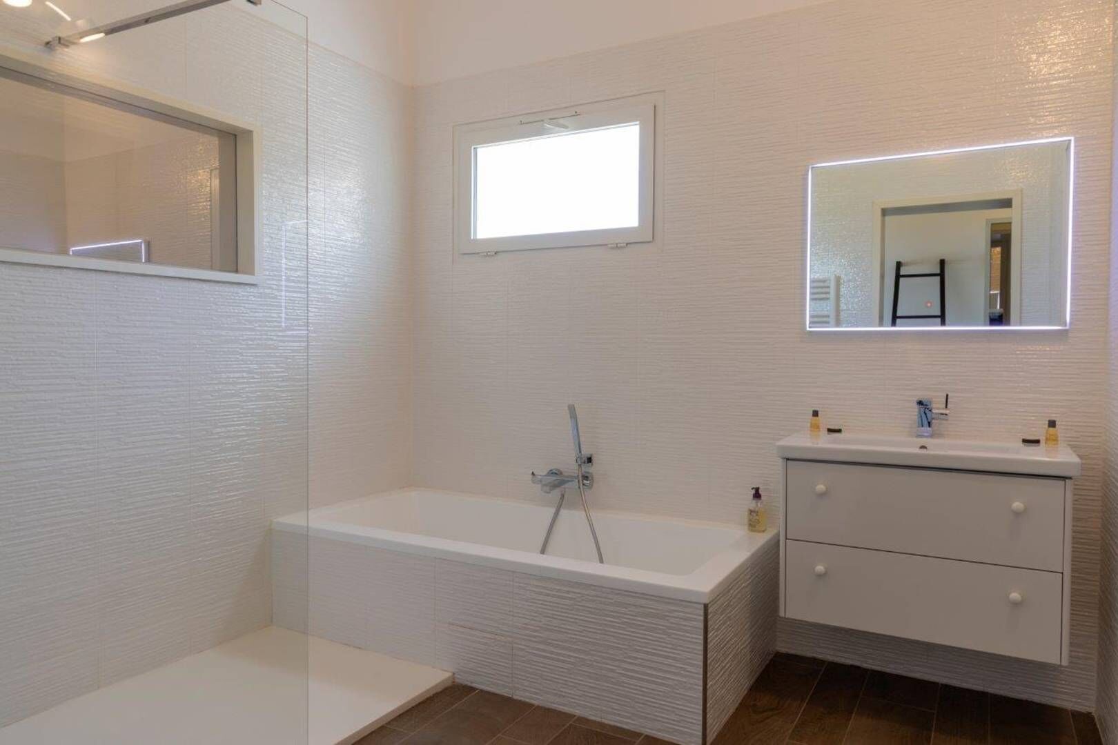 Une salle de bain moderne avec une douche à l’italienne, un meuble-lavabo intégré avec un miroir et une fenêtre au-dessus du lavabo.