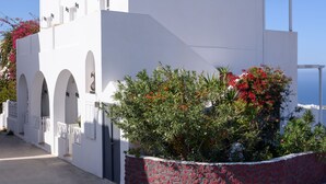 Un bâtiment blanc avec des portes en arc de cercle et un mur de pierre orné de fleurs rouges.