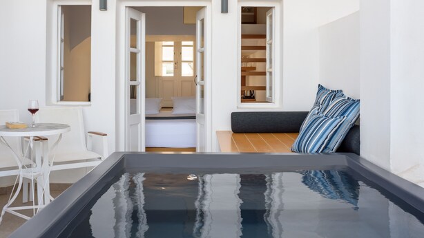 Une chambre moderne dotée d’un grand bain à remous rectangulaire, d’un coin repas blanc avec une table et des chaises, et d’un espace salon confortable avec un canapé et des coussins à rayures.