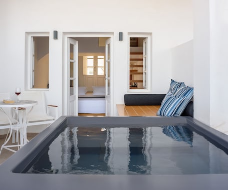 A modern room with a large rectangular hot tub, a white dining area with a table and chairs, and a cozy seating area with a sofa and striped pillows.