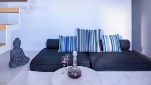 En moderne stue med sofa, puder, et sofabord i glas og en Buddha-figur.