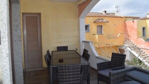 Un balcon avec des meubles en osier, une porte et, au fond, un bâtiment dont le toit est recouvert de tuiles.
